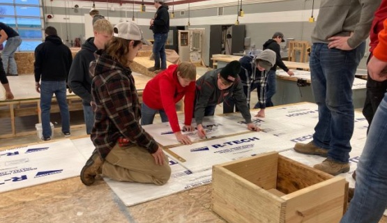 Students work together measuring, marking, and watching two classmates mark insulation to be added to their mock up roof. 