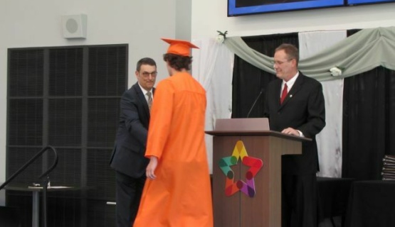 A Coldwater graduate dressed in cap and gown is pictured being called on stage and receiving his career passport at graduation. 