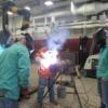 Adult students carefully watch instructor Joe Braun as he demonstrates a welding technique.: Gallery Image 2 