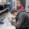A Sophomore works on a circuit under the watchful eye of a REC Tech senior.: Gallery Image 1 