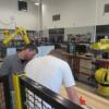 FANUC Robotics instructor Luke Zinc helps a student with a robot.: Gallery Image 1 