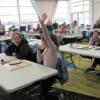 A student, with her parent at their crafting table, raises her hand to answer a question.: Gallery Image 1 