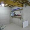 Unfinished basement with safe room, utilities and shelving, egress window, and staircase to garage.: Gallery Image 5 