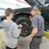 An auto tech student gives instructions for removing the lug nuts on a wheel. 