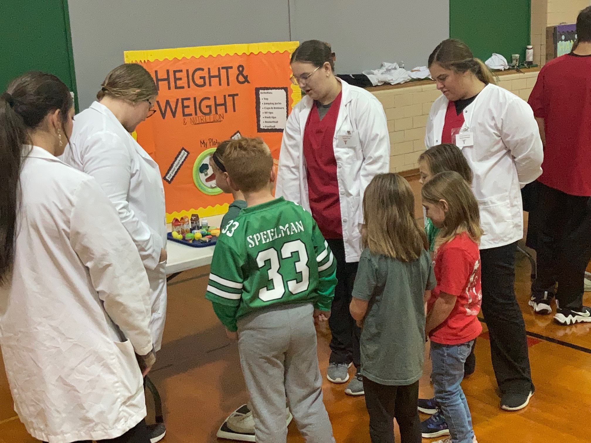 Tri Star Med Prep students in white coats talk to Celina primary school students at their height and weight booth.: Featured Image 1 