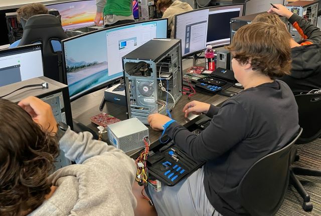An IT/Cybersecurity student is seen putting computer parts back into his computer tower.: Featured Image 1 