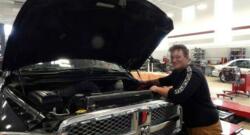 This auto tech student is happily checking under the hood of a truck that needs repair. 