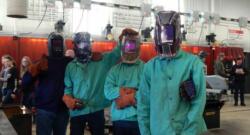 Four welders stand shoulder to shoulder in the welding protective gear. 