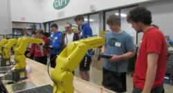 REC Tech students working teach pendants at a row of FANUC robots. 